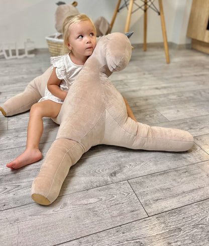 Toddler sitting on large cream soft toy pegasus with gold accents in nursery