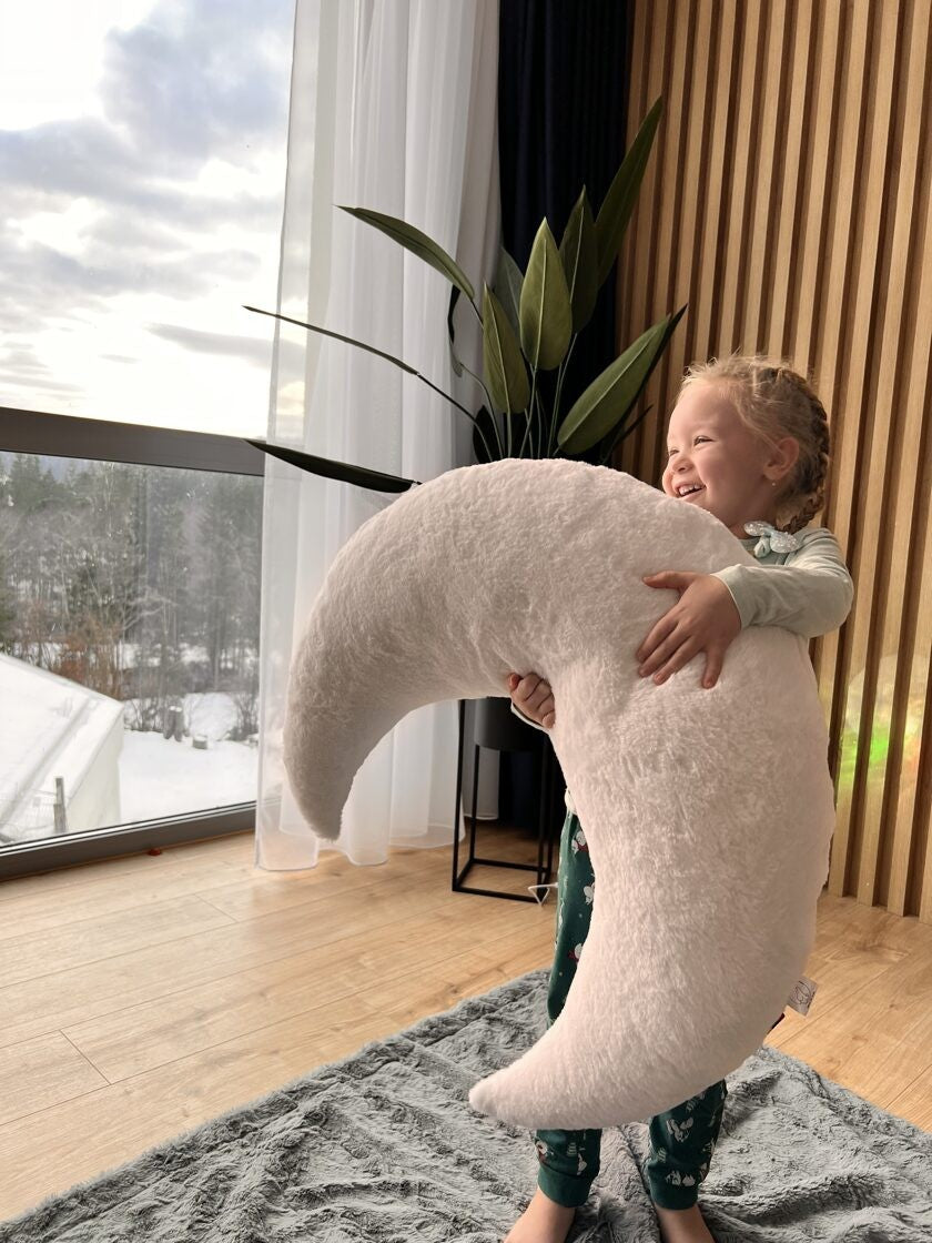 Toddler holding and hugging giant white moon pillow, demonstrating generous size
