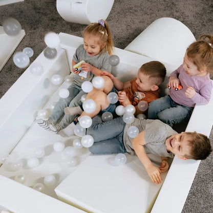 Four young children playing together in white ball pit filled with soft play balls