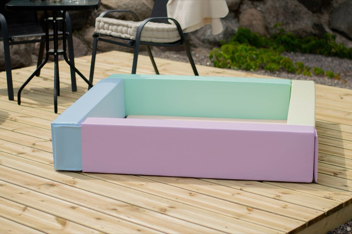 Empty light pastel ball pit showing blue, pink, yellow, and mint green foam sides with entry steps outdoors