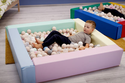 Toddler playing inside light pastel foam ball pit filled with soft play balls, demonstrating easy access