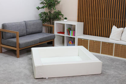 White soft play ball pit positioned in modern living room with gray sofa