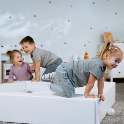 Three young children playing and climbing in white soft foam ball pit