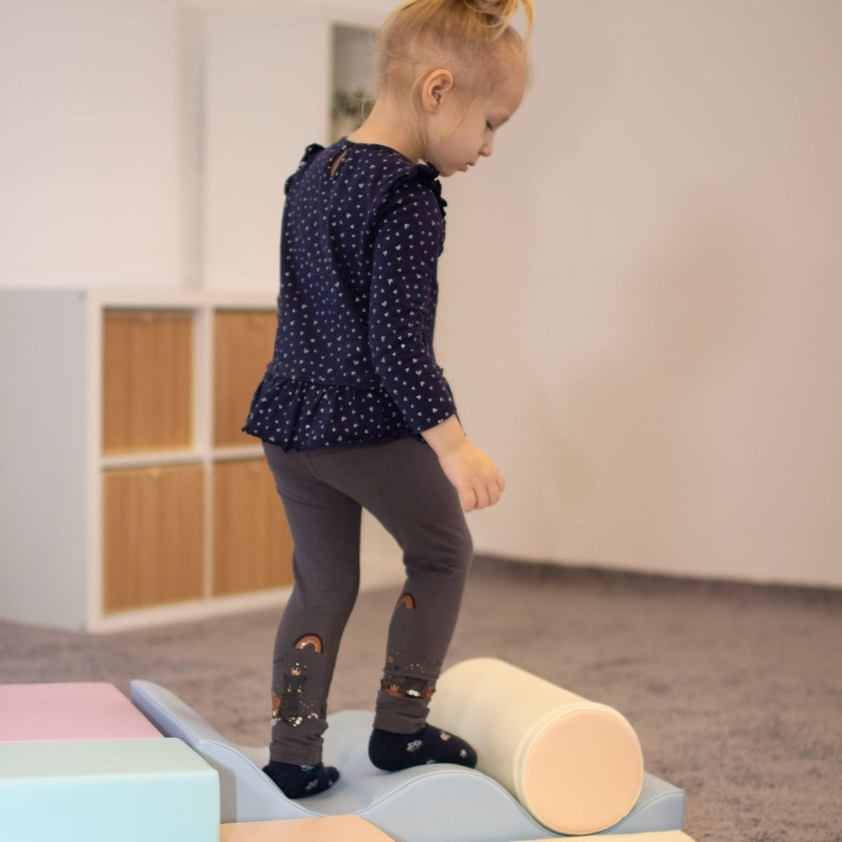 Toddler balancing on cream foam cylinder while standing on pastel foam blocks