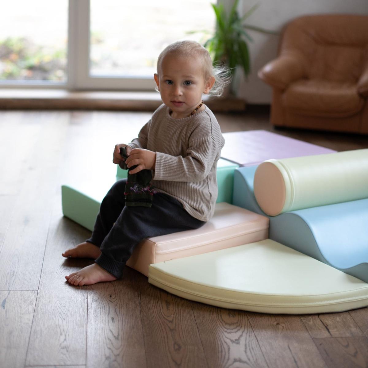 Toddler sitting on assembled light pastel foam block structure with ramp and cylinder