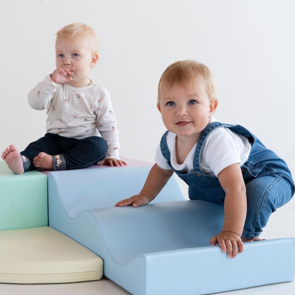 Two toddlers playing on assembled light pastel foam block structure from side view