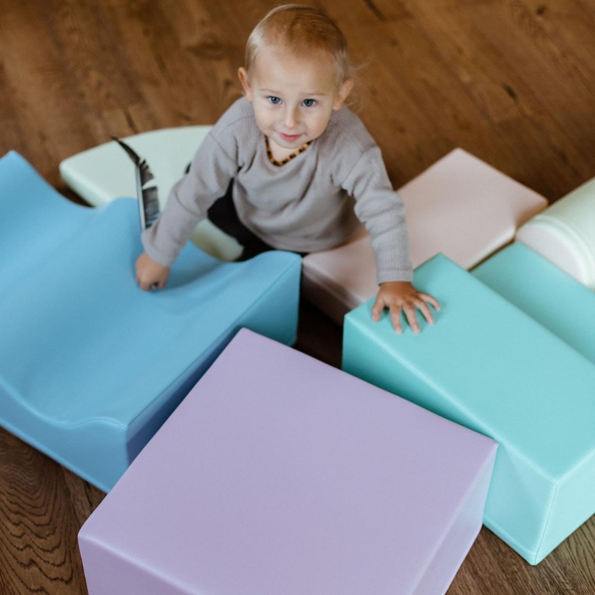 Close-up of toddler on light pastel foam oval mat and block structure