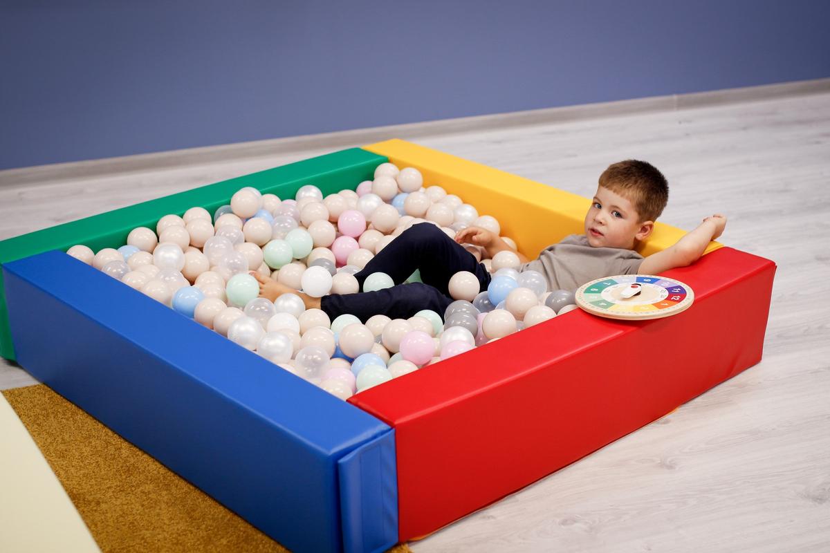Child relaxing in IGLU multicolor soft foam ball pit filled with balls – sensory play indoors