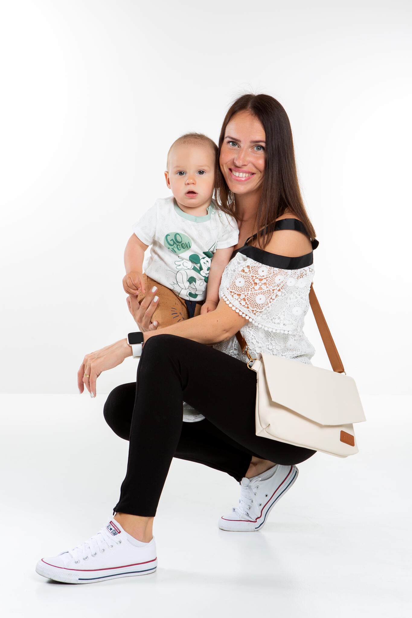 Mom crouching with infant wearing cappuccino vegan leather baby handbag
