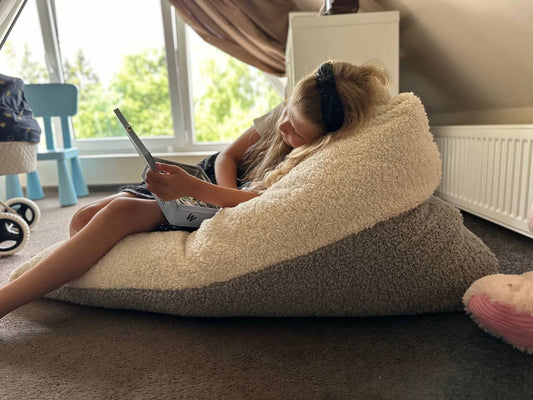 Child lounging on cloud-soft sherpa bean bag chair while using laptop