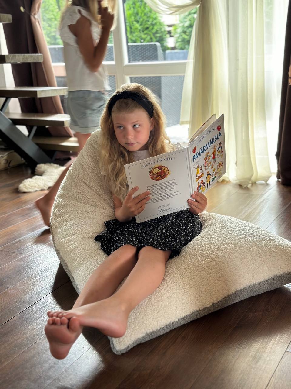 Girl curled up in two-tone sherpa bean bag reading a book indoors