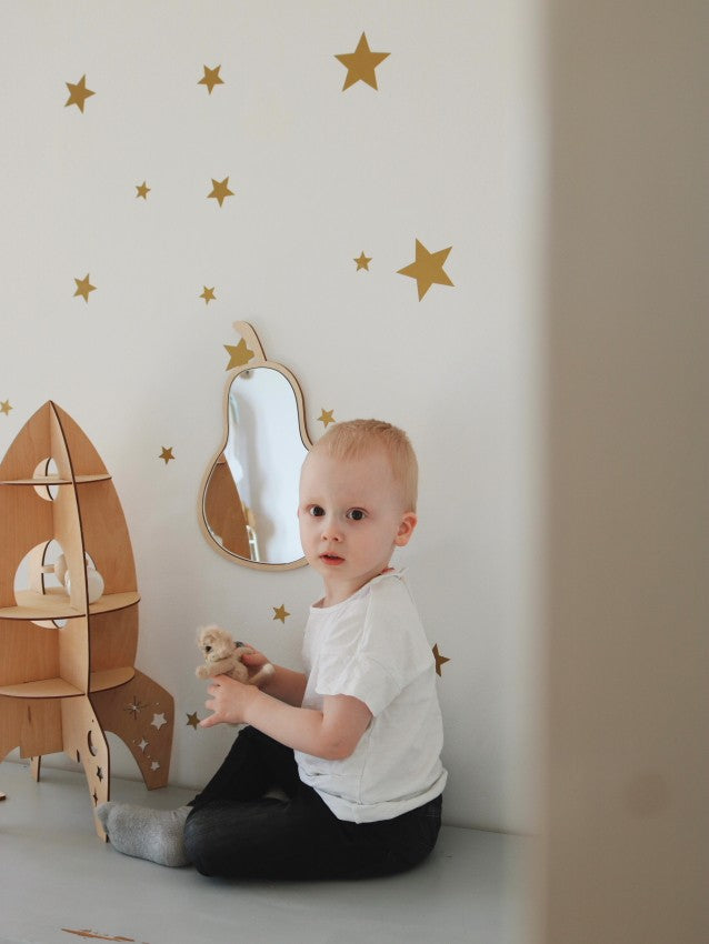Child sitting beside pear mirror wall hanging in bright nursery with star wall decorations