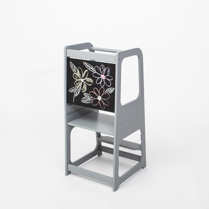Gray wooden kitchen helper tower with blackboard panel featuring flower chalk drawings