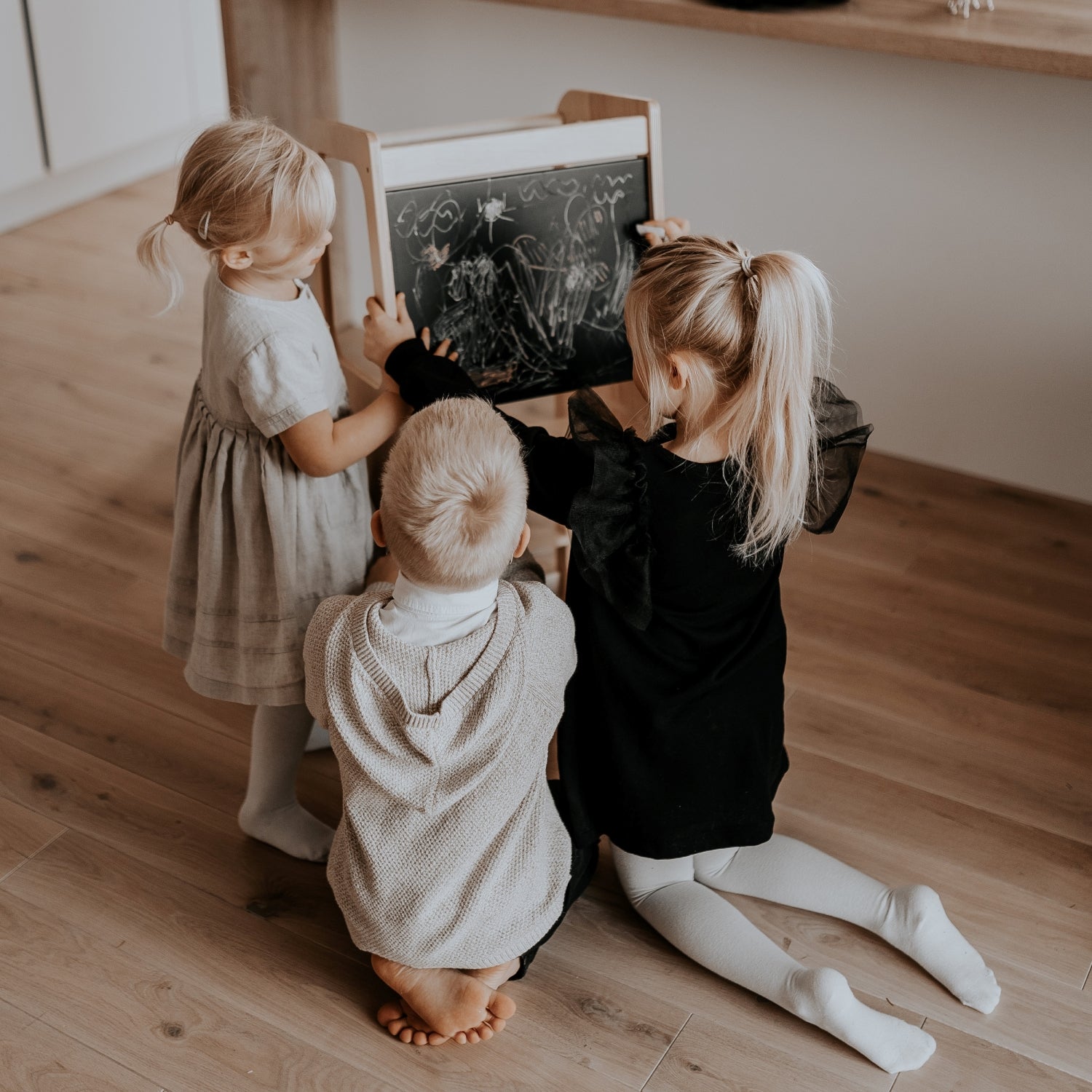 Three children playing together at blackboard panel on wooden kitchen helper tower