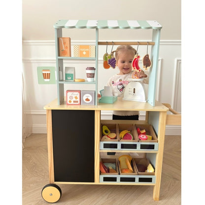 Young child playing shopkeeper at wooden food truck with chalkboard menu