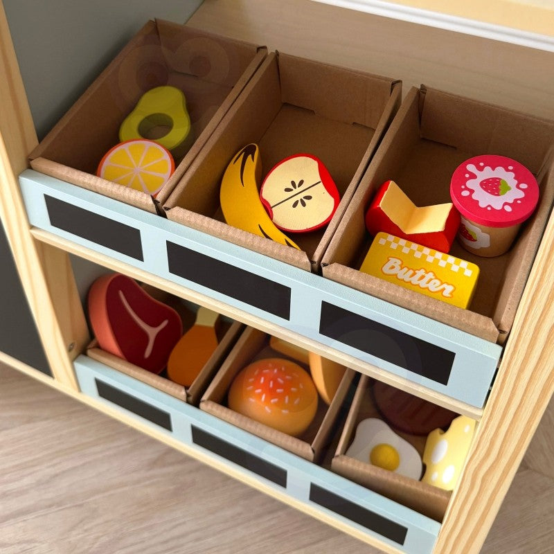 Storage drawers containing wooden play food pieces including avocado, lemon, and meat cuts