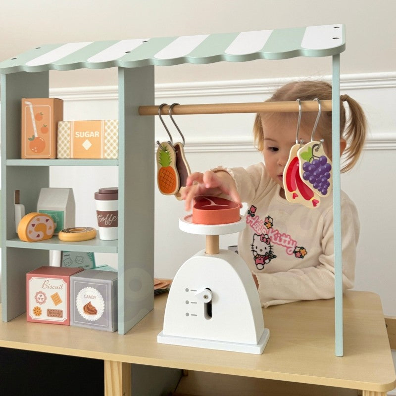 Young child reaching toward wooden food truck stand with hanging pretend food