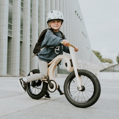 Child in helmet riding white and natural wood leg&go pedal bike outdoors