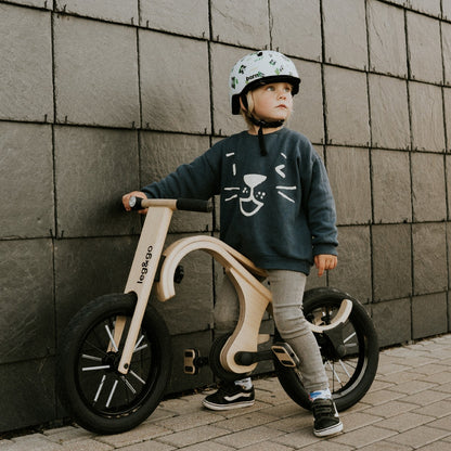 Toddler standing with leg&go pedal bike against textured wall backdrop