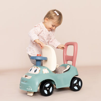 Toddler sitting on turquoise ride-on pusher with pink handle and horn, demonstrating seated play