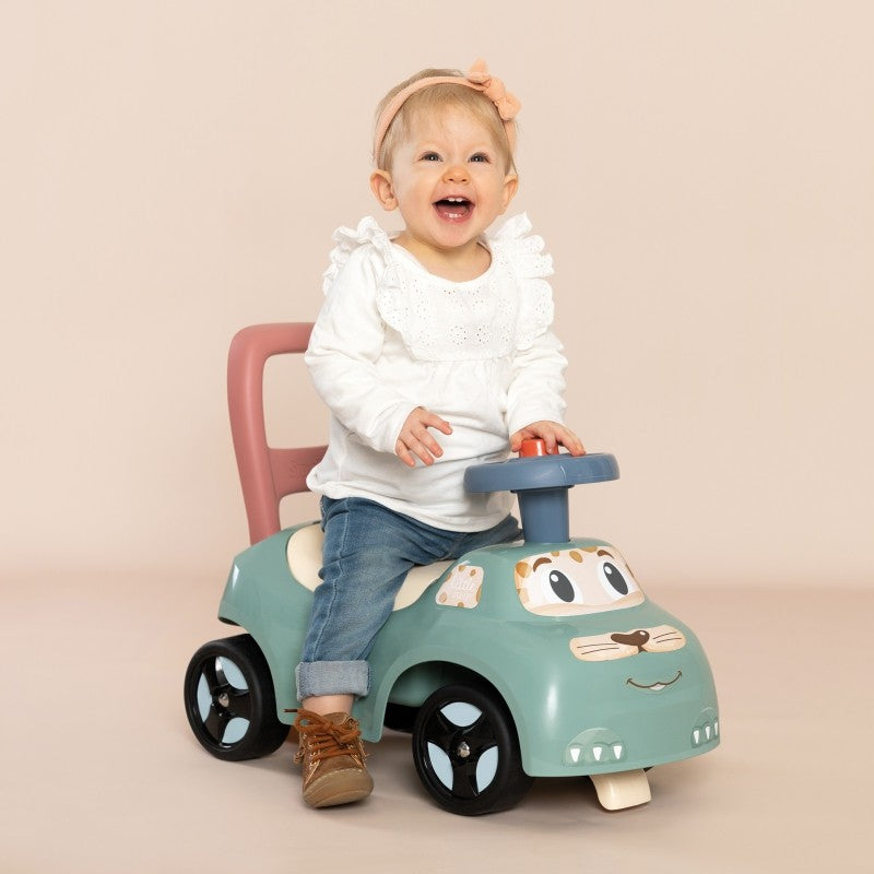 Toddler gripping blue horn while seated on turquoise ride-on with pink backrest