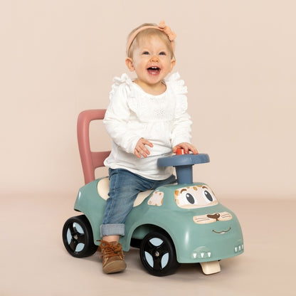 Toddler gripping blue horn while seated on turquoise ride-on with pink backrest