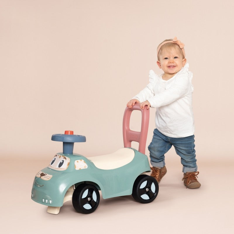 Toddler pushing turquoise ride-on car from behind using pink handle bar