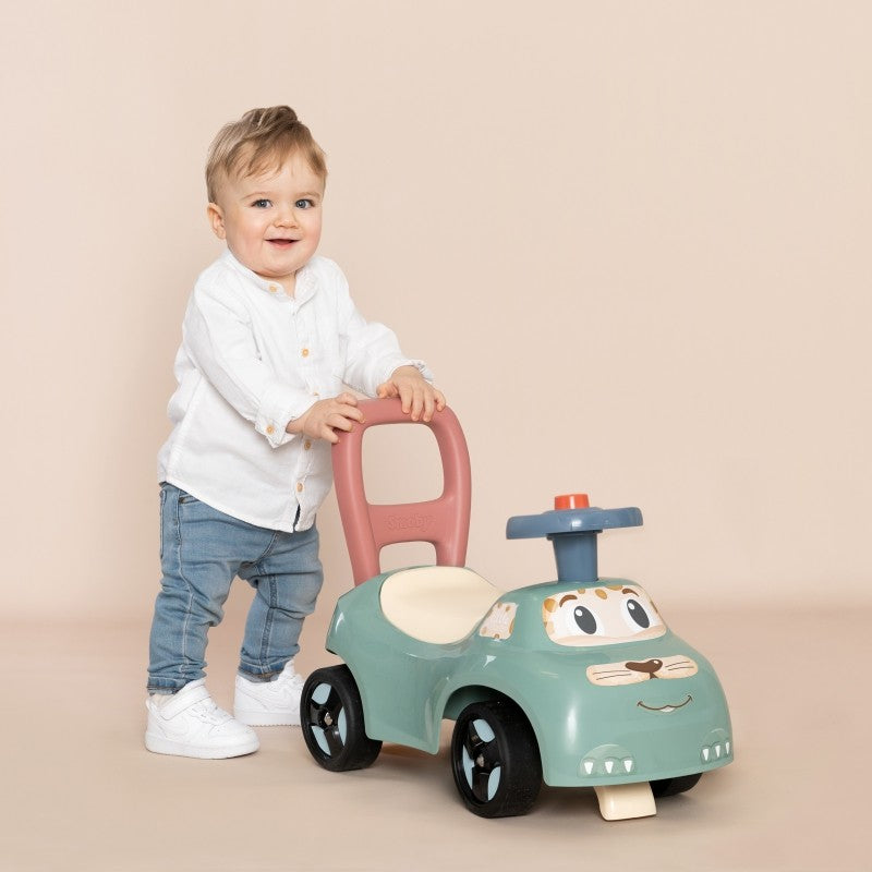 Child standing beside turquoise ride-on pusher holding pink backrest handle