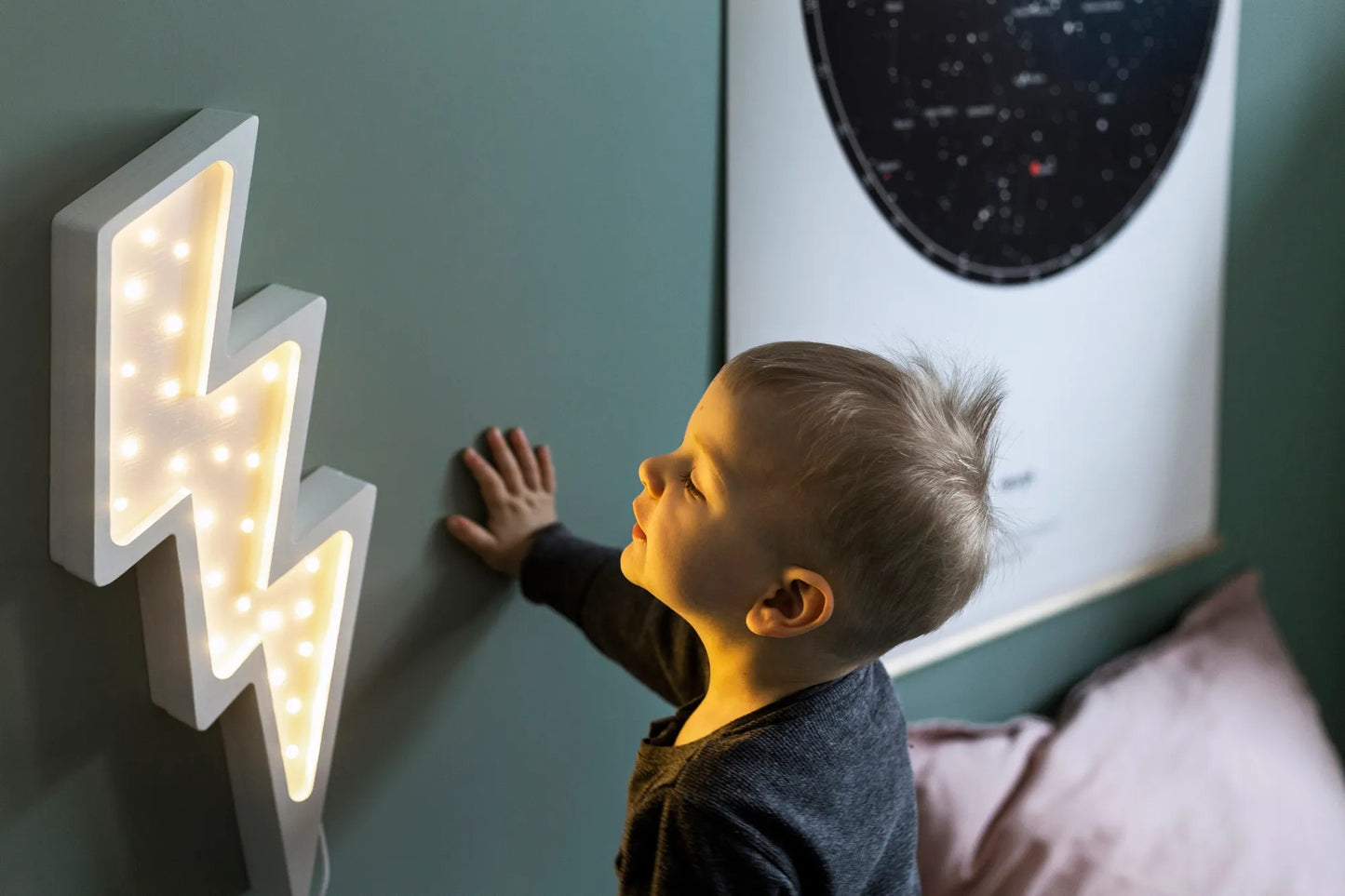 Child reaching toward white bolt lamp on wall with remote control visible