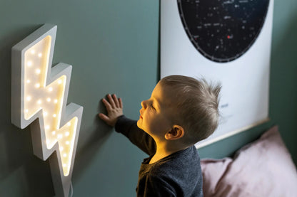 Child reaching toward white bolt lamp on wall with remote control visible