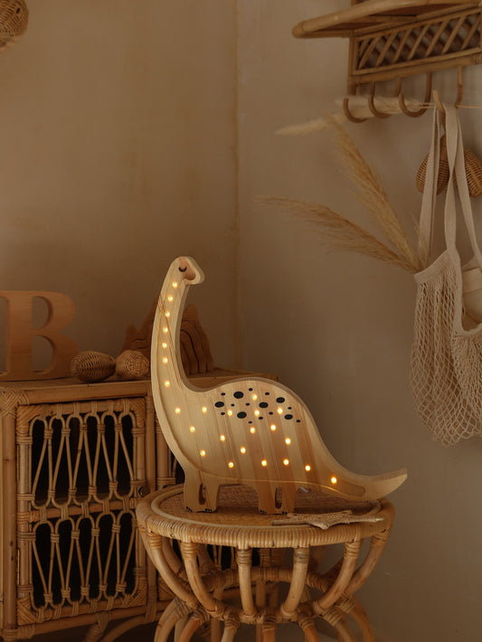 Natural wood diplodocus lamp with warm white LED lights glowing on neck and body, displayed on woven side table in styled