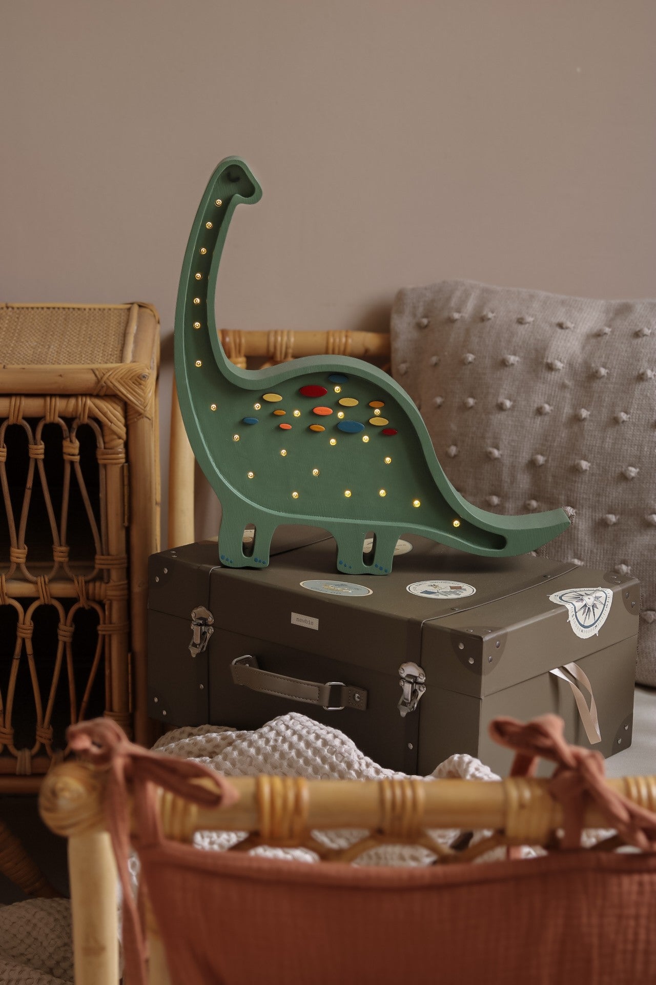 Dark green diplodocus night light with illuminated LED dots, styled on black suitcase in bedroom setting
