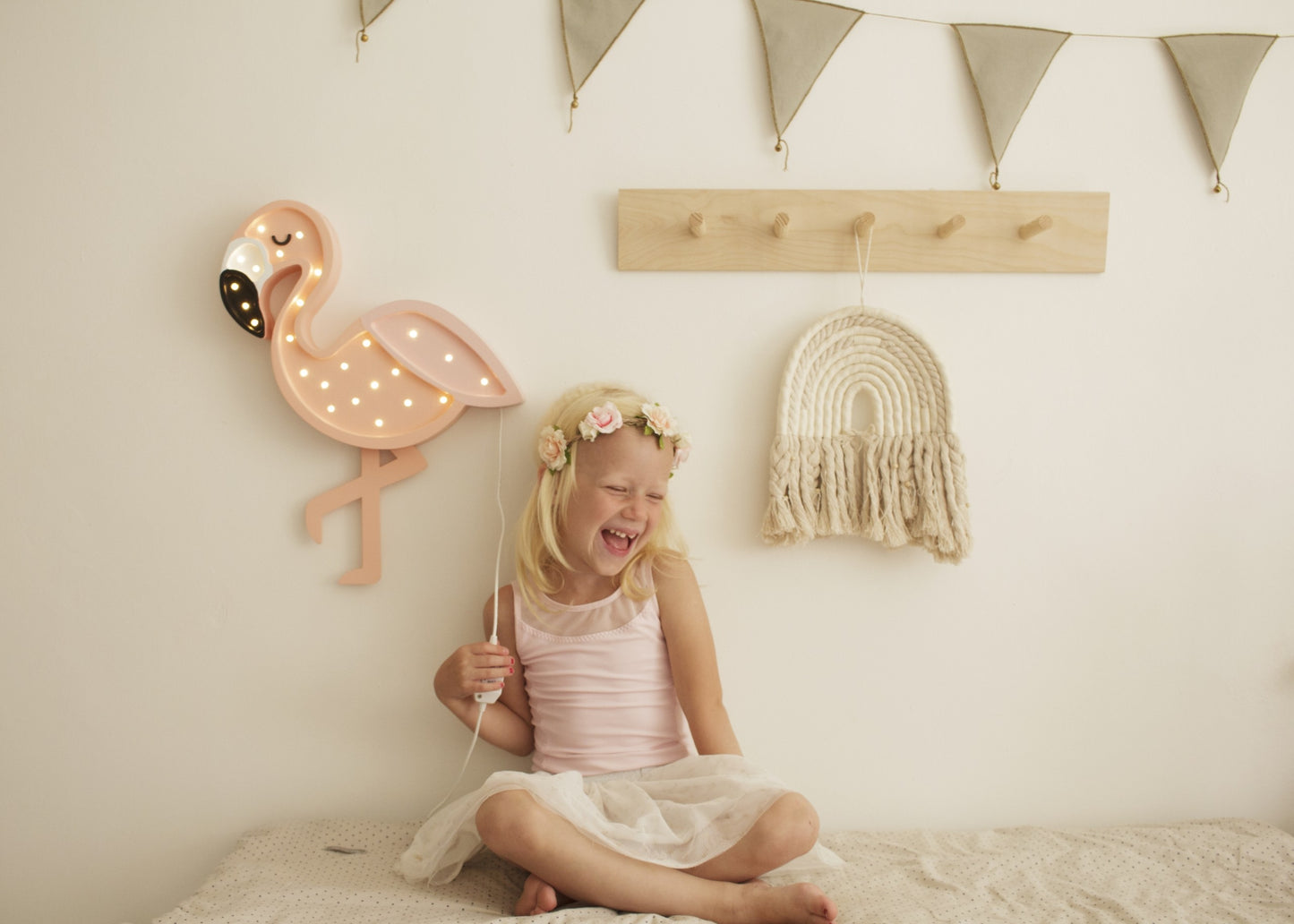 Child holding illuminated flamingo lamp in decorated bedroom with bunting and wall shelves