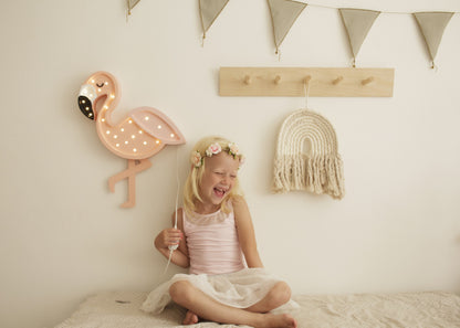 Child holding illuminated flamingo lamp in decorated bedroom with bunting and wall shelves
