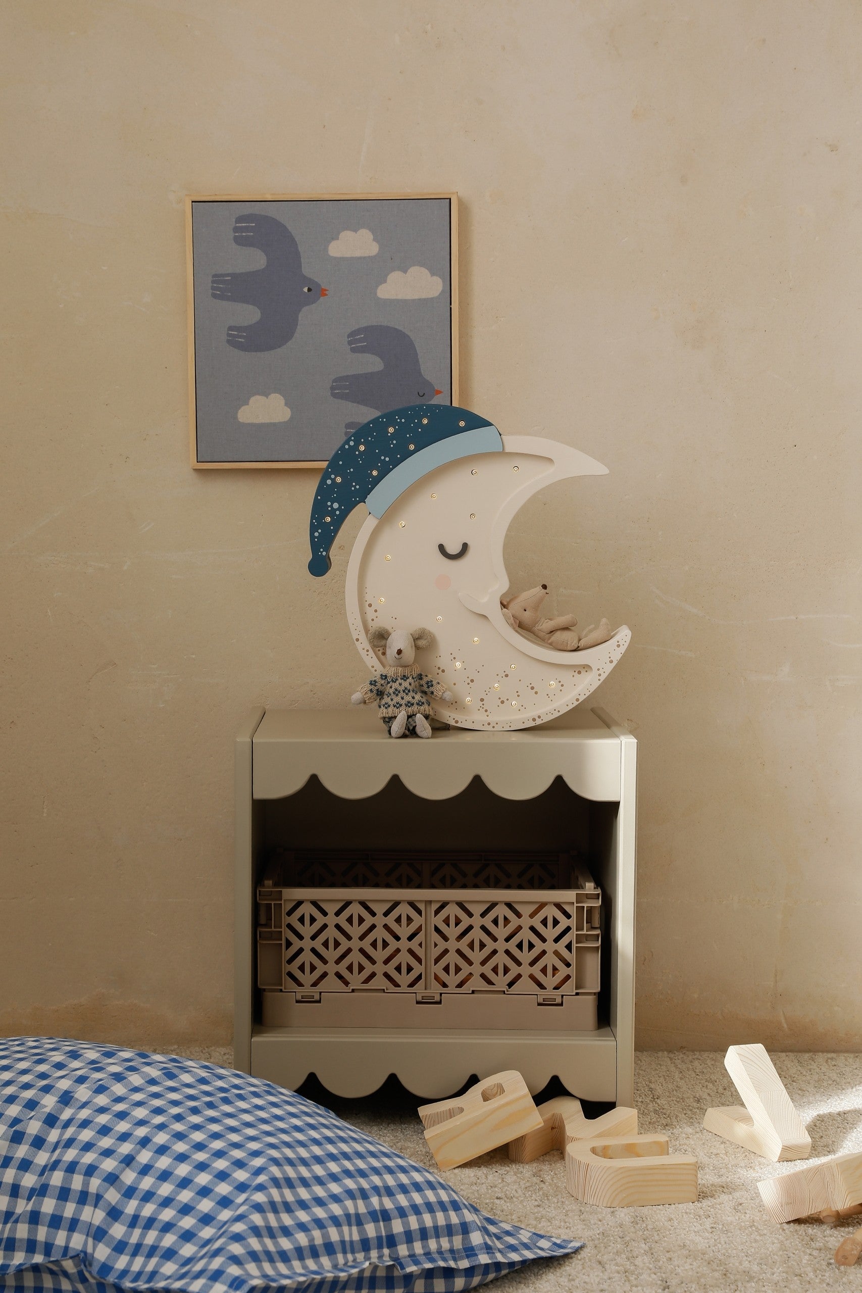 Moon lamp displayed on bedroom dresser beside stuffed toys and wall art above child's bed