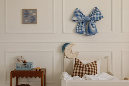 Crescent moon lamp mounted on bedroom wall above bed with decorative pillows and wall art