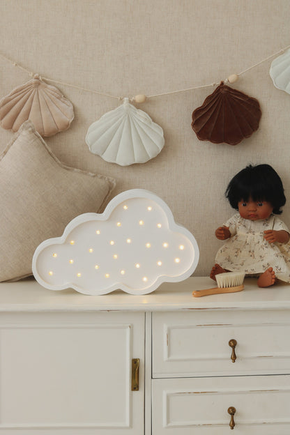 White cloud lamp with warm LED lights on nursery dresser next to decorative shell garland