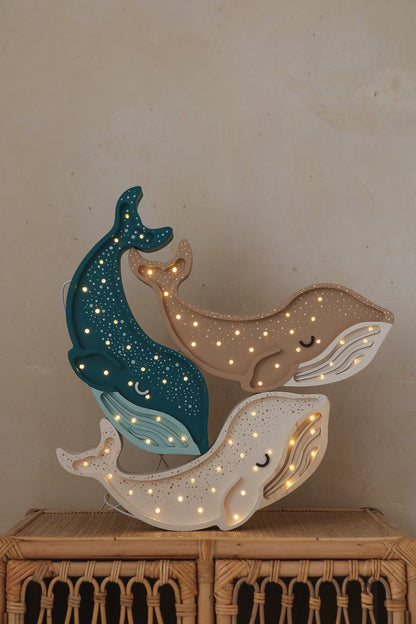 Little Lights whale lamp stacked display with dark teal, tan and cream wooden whale shapes lit with warm white LED lights