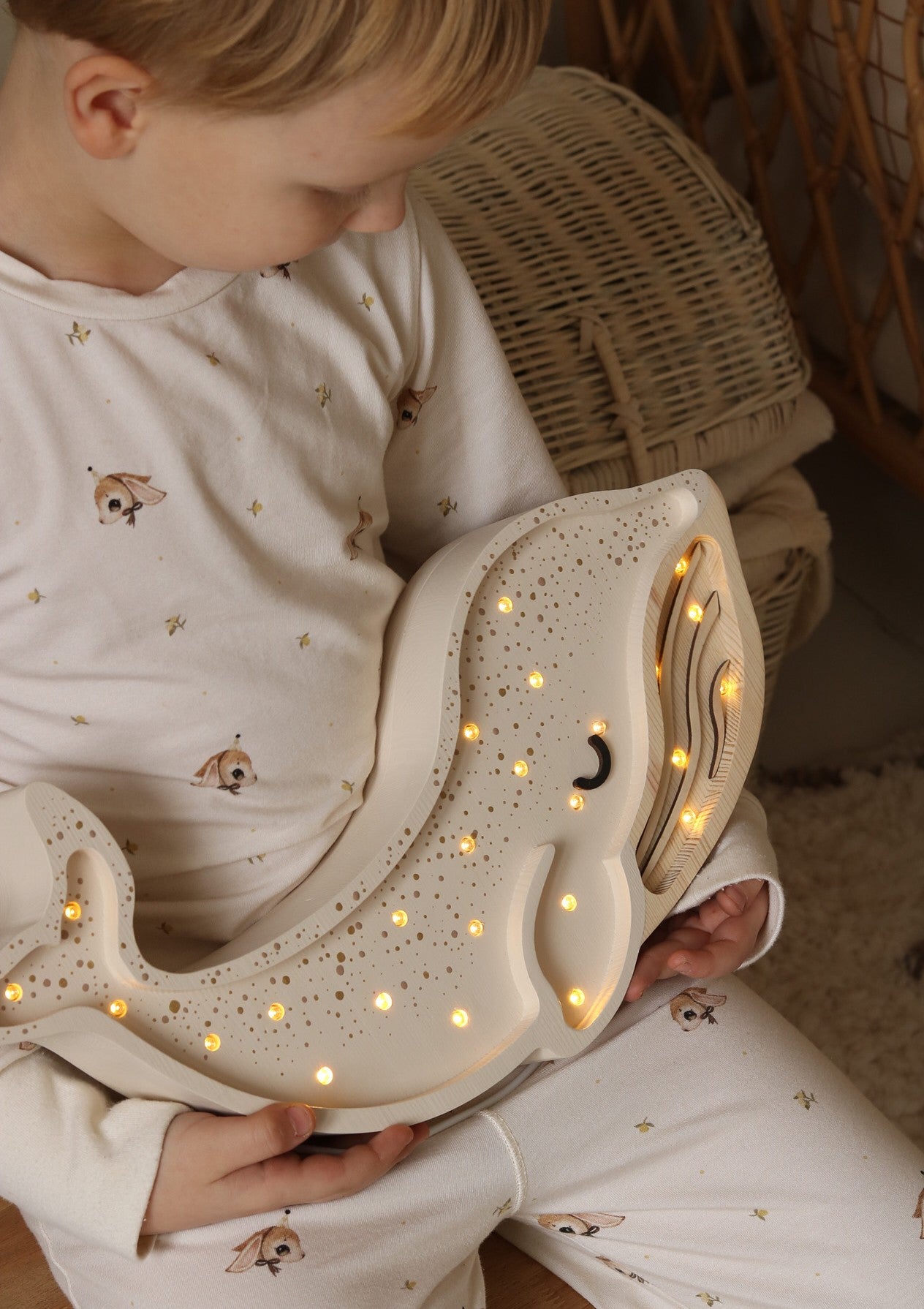 Child holding light cream whale lamp showing warm white LED lights and wooden texture details