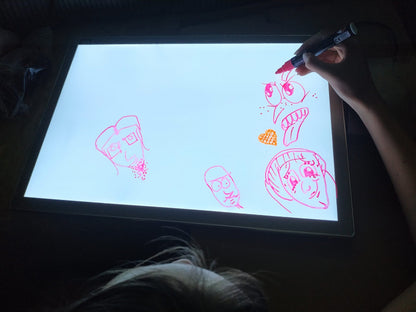 Close-up of child drawing pink and orange sketches on lit light board