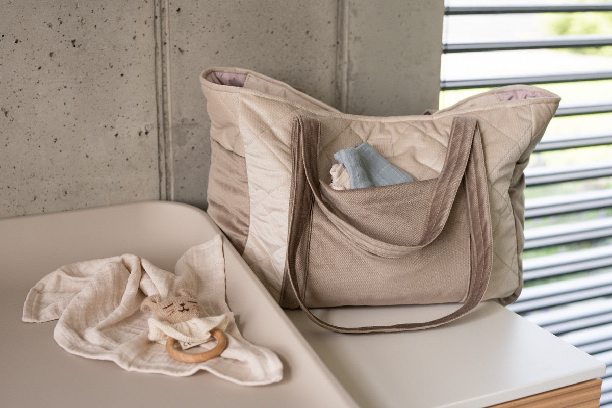 Beige velvet weekender bag displayed on table with organized inner pockets holding baby items