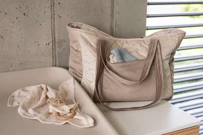 Beige velvet weekender bag displayed on table with organized inner pockets holding baby items
