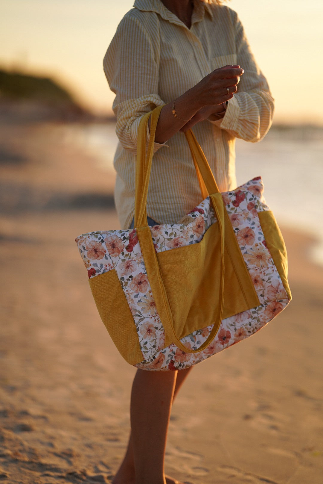 Woman carrying floral weekender bag on beach at sunset, side view