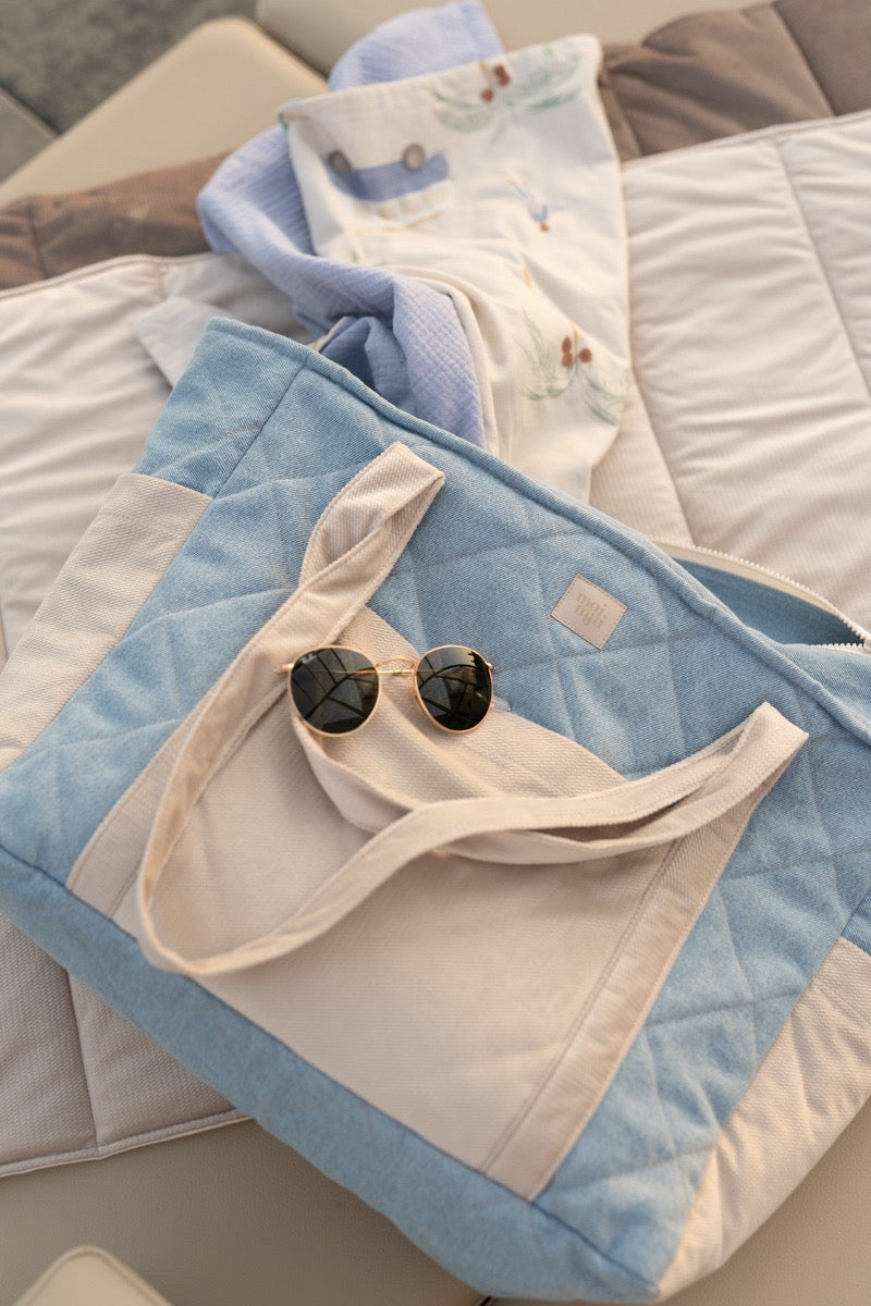 Jeans weekender bag styled flat on bed displaying outer pocket storage with sunglasses and items