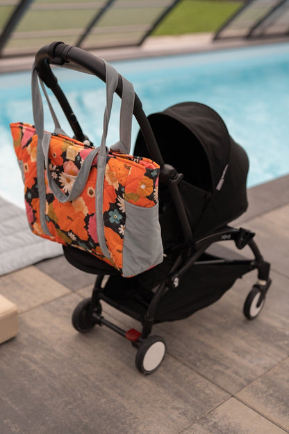 Mom weekender bag attached to black stroller at pool with beach setting behind