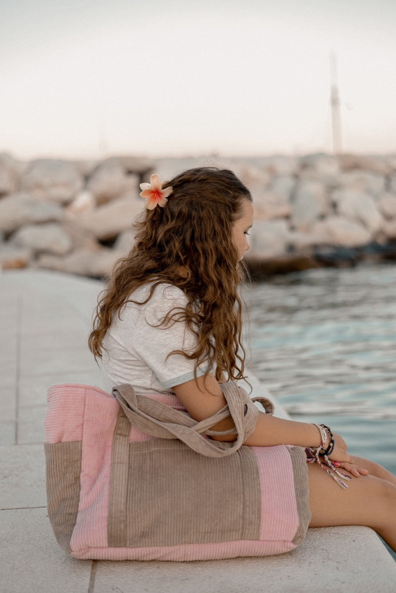 Woman sitting on waterfront holding pink coffee velvet cotton weekender bag