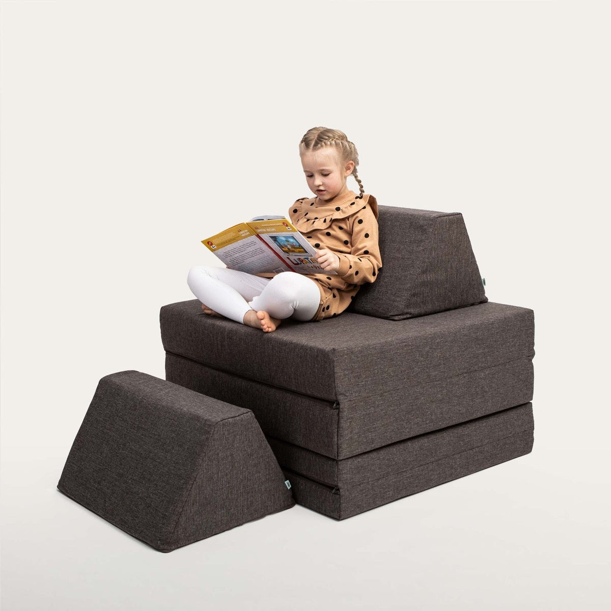 Girl playing on dark brown foam furniture built into a multilevel configuration with reading space