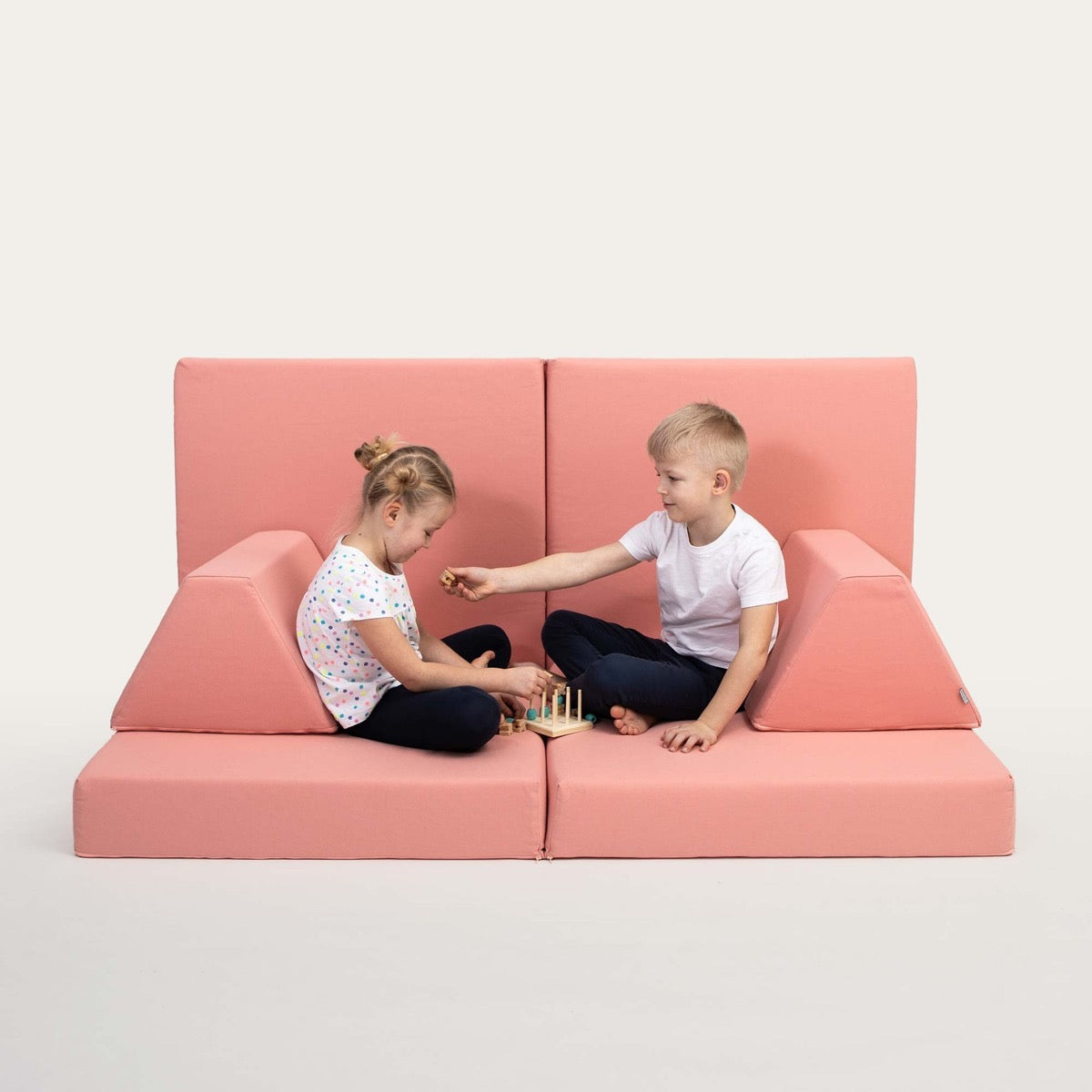 Two children sitting on salmon pink foam sofa configuration playing together indoors