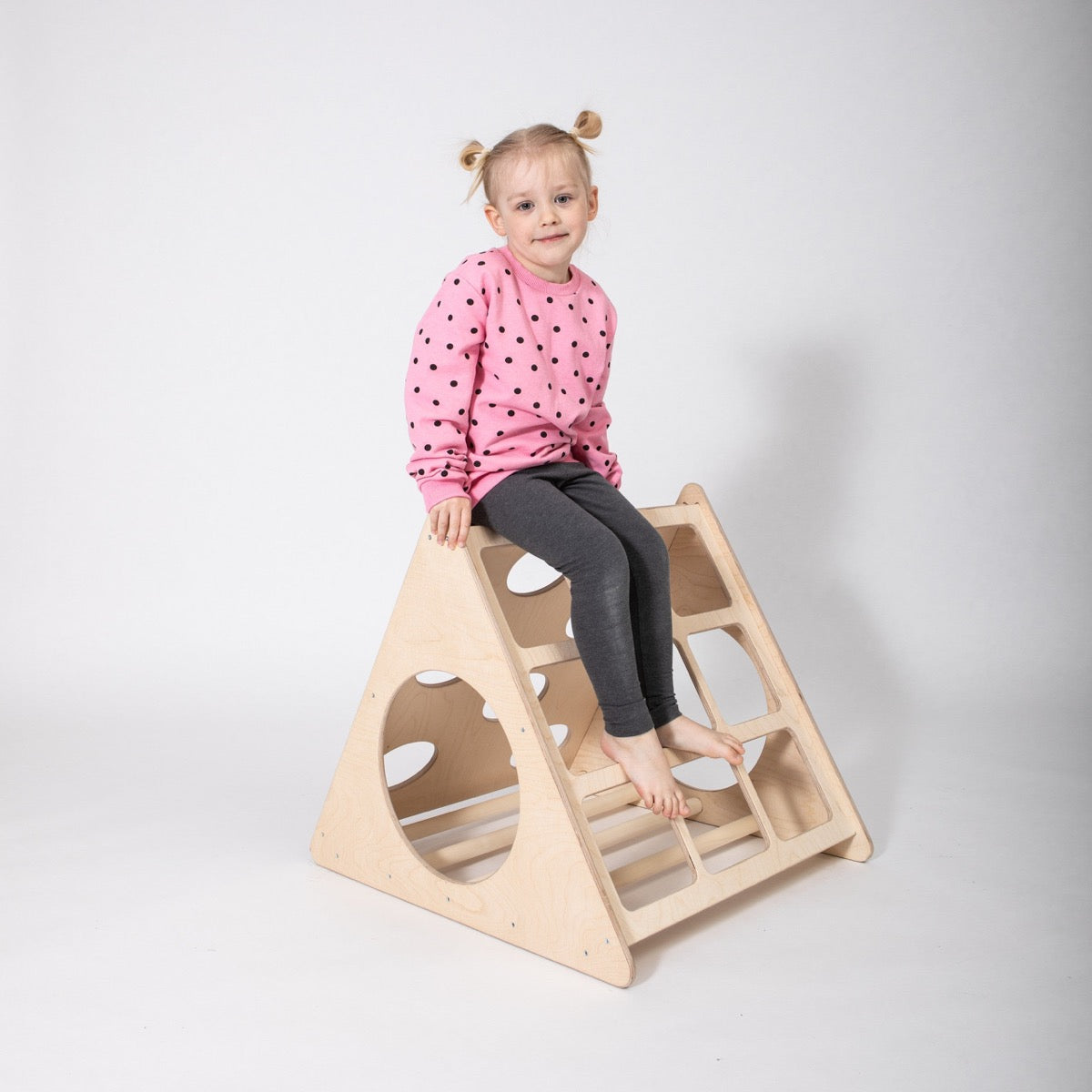 Toddler sitting on top of wooden climbing triangle with cutout handles
