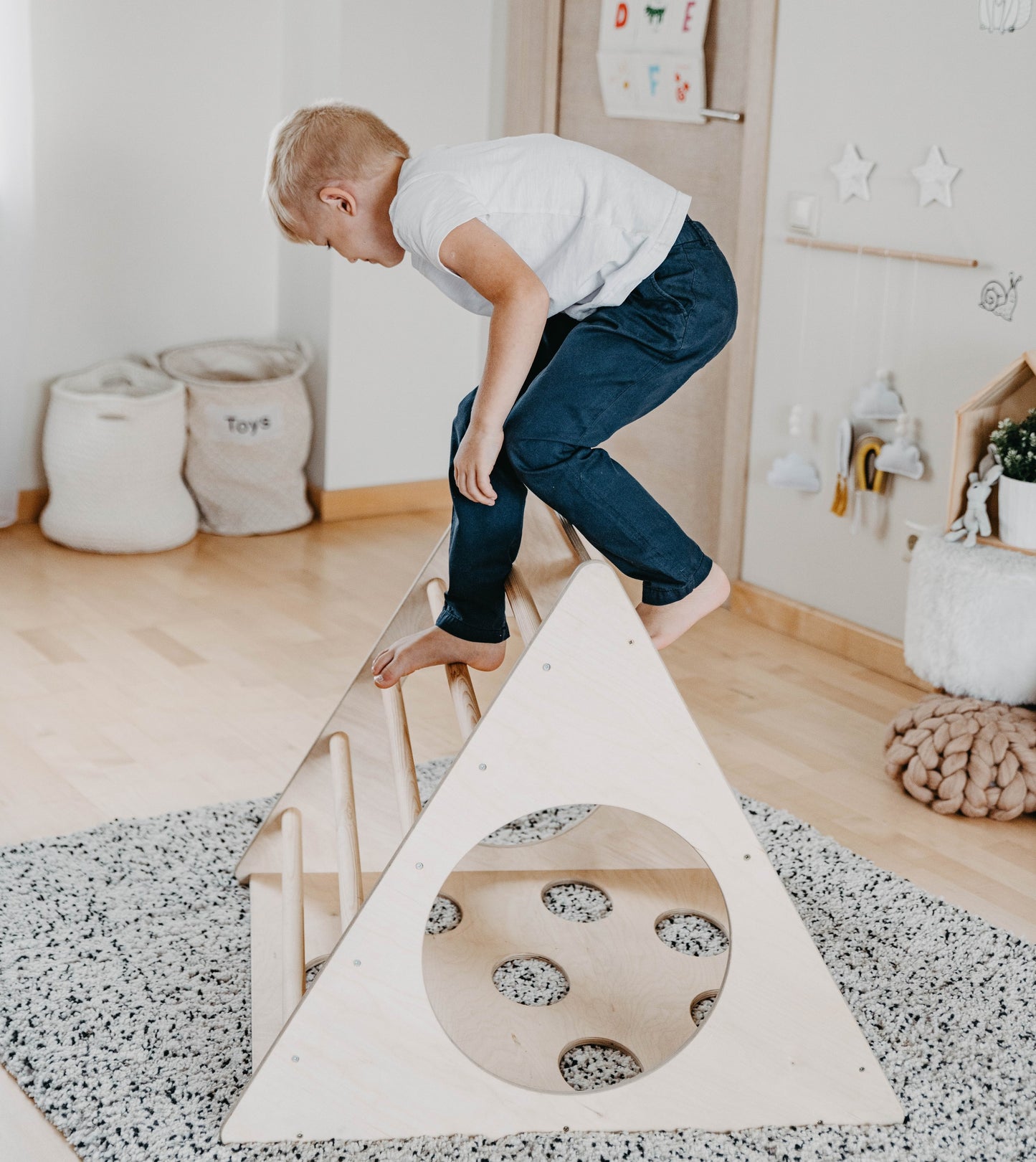 Boy climbing up wooden triangle in home play space with storage baskets